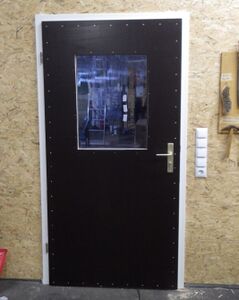 eingebaute Tür zum Gemeinschaftsraum mit wiederverwendetem Polycarbonatfenster und deutlich sichtbaren gelb passivierten Spanplattenschrauben